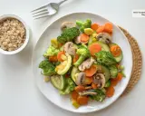 Un colorido salteado de verduras con brócoli, zanahoria, calabacín y champiñones, servido junto a un tazón de arroz integral.