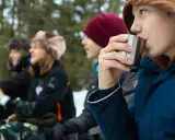 Barn njuter av fika under friluftsdag aktiviteter i snöig skog. En pojke dricker ur en metallmugg.