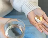Dłoń z kilkoma tabletkami i kapsułkami, szklanka wody. Czy to objawy nadmiaru cynku?