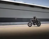 Motociclista con casco y chaqueta de cuero sobre una moto estilo cafe racer, en movimiento rápido por una carretera. El carmet a2 es su compañero de aventuras.