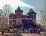 Drewniany zamek z kamiennymi elementami, otoczony skałami i drzewami. Wspaniałe **Pszczyna atrakcje** dla całej rodziny, gdzie dzieci mogą poczuć się jak rycerze.