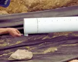 Main tenant applique un produit sur un tuyau blanc pour comment déboucher une canalisation enterrée.