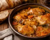 Contramuslos de pollo dorados en cazuela con zanahorias y cebolla, acompañados de pan rústico.
