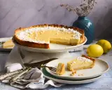 Ein köstliches Zitronentarte Rezept: Eine ganze Tarte und ein Stück auf einem Teller, bestäubt mit Puderzucker. Zwei Zitronen liegen daneben.