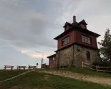 Drewniana wieża widokowa na Luboniu Wielkim, z kamiennym fundamentem, otoczona zielenią i ławkami.