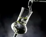 Klarer Grappa wird in ein Glas gegossen. Die Frage "wie viel prozent hat grappa" wird durch die klare Flüssigkeit und die Bläschen im Glas angedeutet.