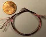 Ein-Cent-Münze neben einem Bündel dünner roter und schwarzer Kabel mit kleinen Lötpunkten.