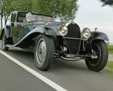 Ein Mann fährt einen glänzenden schwarzen Bugatti Royale auf einer Landstraße. Der Bugatti Royale Preis ist astronomisch, ein Traum für jeden Sammler.