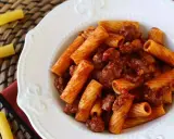 En portion pasta med korv i tomatsås, serverad på en vit tallrik.