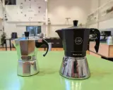 Zwei Espressokocher, ein silberner und ein schwarzer, stehen bereit für den perfekten Espresso auf dem Herd.