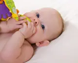 Ein Baby mit blauen Augen erkundet sein buntes Spielzeug. Vielleicht ist es der 19-Wochen-Schub, der ihn so neugierig macht.