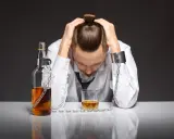 Mężczyzna w kajdanach, przykuty do butelki i szklanki z alkoholem, symbolizuje uzależnienie od piwa i jego niszczycielską siłę.