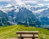 Ławka na tle majestatycznych gór w Grindelwald. Zielone wzgórza i skaliste szczyty tworzą zapierający dech w piersiach krajobraz.