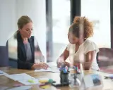 Deux femmes discutent de documents lors d'une réunion. L'une, blonde, porte un blazer sombre. L'autre, aux cheveux bouclés, est en chemisier clair. Leurs mains pointent vers les papiers, comme pour en comprendre le **signification**.