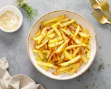 Un plato lleno de crujientes patatas fritas doradas, espolvoreadas con hierbas frescas. ¡Perfectas para compartir!