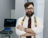 Ortopeda w okularach i ozdobnych szelkach stoi przed aparatem USG.