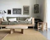 Une idée table basse fait maison en bois brut, posée sur un tapis tressé, devant un canapé vert et des tableaux abstraits.