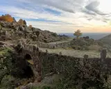 Herbstliche Farben in der Sierra de Gata. Ein alter Steinbogenbrücke, überwuchert von Efeu, führt durch eine felsige Landschaft.