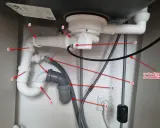 Instalacja hydrauliczna pod zlewem, pokazująca jak zrobić odpowietrzenie WC. Widoczne rury, syfon i podłączenie do gniazdka.