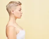 Perfil de una mujer joven con un moderno corte pixie rubio, luciendo un top blanco.