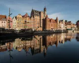 Gdańsk atrakcje: zabytkowy żaglowiec cumuje przy Motławie, w tle kolorowe kamienice i Żuraw. Odbicia budynków w wodzie.