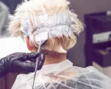 Friseur mit Handschuhen trägt Bleichmittel auf blondes Haar auf. Der Prozess des Haare bleichen beginnt.