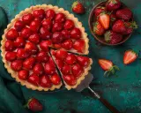 Une magnifique tarte aux fraises, garnie de fruits rouges brillants, est prête à être dégustée. Une part a été coupée, révélant la crème onctueuse.