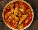 Un saporito pollo con peperoni in umido, cotto in una casseruola verde su un tavolo di legno scuro.