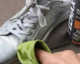 Srebrne buty czyszczone zieloną ściereczką obok puszki z wazeliną techniczną.
