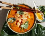 Miseczka zupy tom yum z krewetkami, ozdobiona ziołami, pałeczki i łyżka.