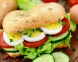 Pyszne kanapki z jajkiem, pomidorem, ogórkiem i sałatą na chrupiącej bułce. Idealne na śniadanie lub lunch.