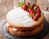 Gâteau génoise fraise, garni de crème, confiture et fruits rouges frais, saupoudré de sucre glace.