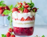 Verrine fraise fromage blanc, un délice estival en couches de génoise, crème et fruits rouges frais, décorée de fraises et de fleurs.