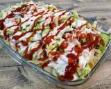 Kapsalon z kurczakiem, sałatą, pomidorami, ogórkiem i sosami w szklanej misce.