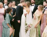 A wedding party celebrates as the bride and groom kiss. The groomsmen attire is classic black tuxedos.
