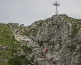 Grupa turystów wspina się po skalistym zboczu Giewontu w kierunku krzyża.
