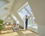 Frau öffnet Dachfenster in hellem Dachboden-Yoga-Raum. Hier darf man Dachboden als Wohnraum nutzen und schafft sich eine Oase.