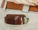 Brązowy portfel z kartami i banknotami w tylnej kieszeni spodni. To symbol oszczędności i strategii franszyza redukcyjna.