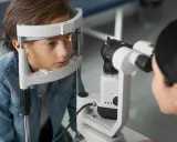 Chłopiec podczas badania wzroku. Okulista wykonuje biometrię oka, analizując jego strukturę.