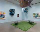Abstract paintings and fabric sculptures adorn the walls of the Lanoue Gallery, with benches placed on a patch of artificial grass.
