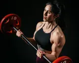 Eine starke Bodybuilderin Frau hebt eine Hantel. Ihre Muskeln sind deutlich sichtbar.