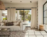 Arredare una casa al mare: divano bianco, cuscini naturali, lampade in rattan e vista su piscina e palme.