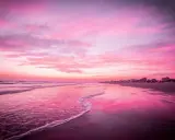 Spiaggia di Riccione immersa nel rosa della Notte Rosa, con il mare calmo e il cielo infuocato.