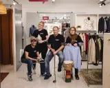 Fyra personer poserar i en butik med kläder och föremål. En kvinna håller en vas, en man en golfklubba, och en annan kvinna en ljusblå hoodie. De representerar hållbart second hand.