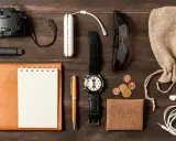 Zestaw EDC: aparat, pendrive, notes, długopis, zegarek, okulary, monety, portfel, słuchawki i woreczek.