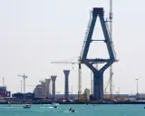 Construcción de un puente con pilares de hormigón y grúas, sobre el mar.
