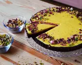 Wyjątkowa tarta pistacjowa, udekorowana płatkami róż i orzechami, kusi swoim wyglądem. Obok miseczki z pistacjami.