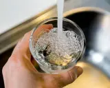 En hand håller ett glas som fylls med vatten från en kran. Bubblor bildas i vattnet, vilket kan tyda på klor i dricksvatten.