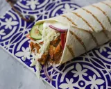 Pyszny kebab w picie z soczystym mięsem, chrupiącą kapustą, pomidorem, ogórkiem i czerwoną cebulą, podany na ozdobnym talerzu.
