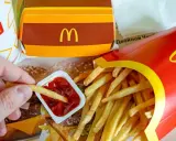 Ręka zanurza frytkę w keczupie. Obok pudełko z frytkami i burgerem. McDouble kcal to smak, który znasz.